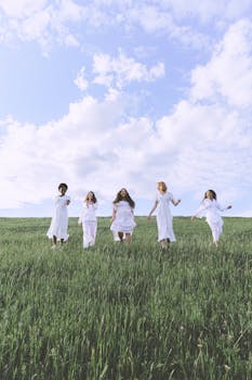 五名穿着白色连衣裙的女子在草地上快乐地奔跑，天空多云