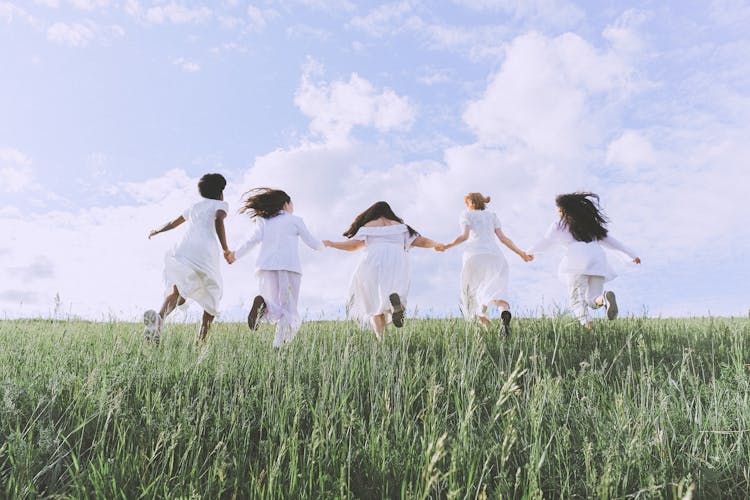 Group Of Women Running On Green Grass Field