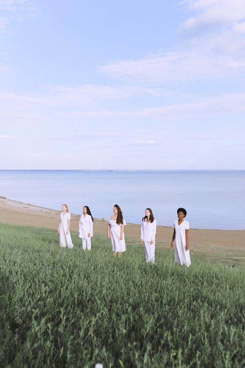 Women In White Standing on Green Grass Field Near Body of Water