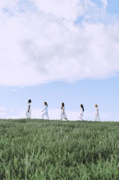 五名白衣妇女走在明亮的蓝天下，脚下是郁郁葱葱的绿色田野