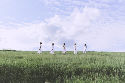 *+&*Women in White Dresses Standing on Green Grass Field Under Cloudy Sky