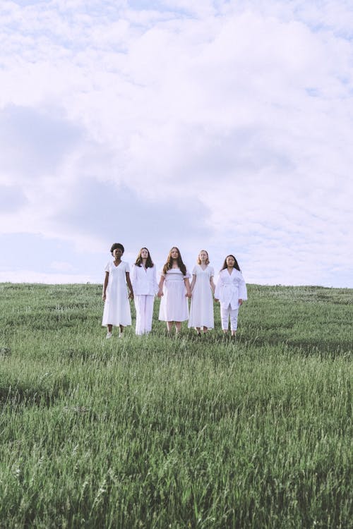  Women Holding Hands While Standing on Green Grass Field Under White Clouds