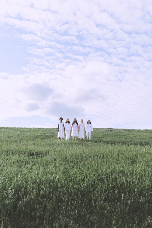 Women Standing on a Grass Field Under White Clouds