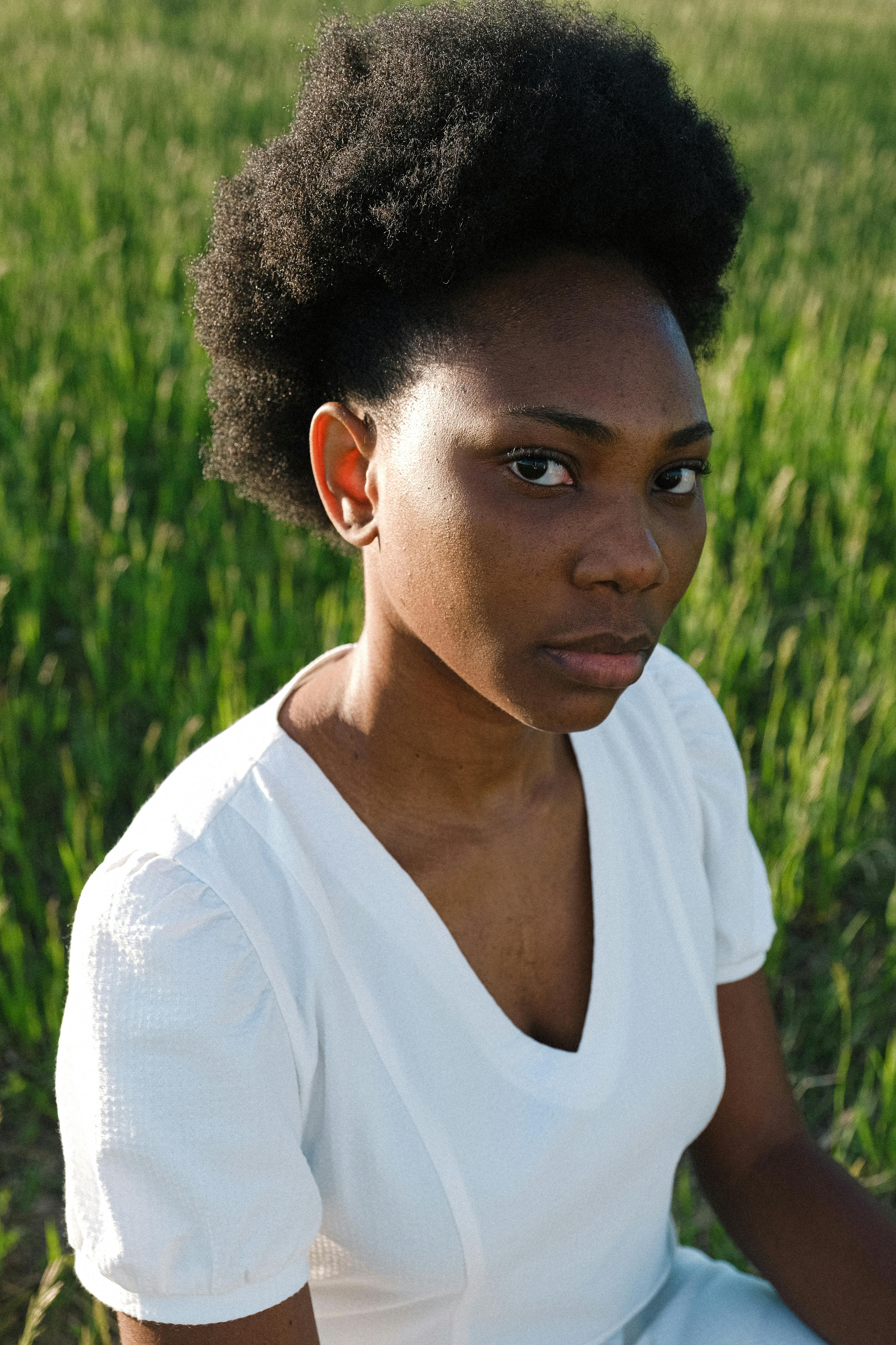 A young African woman in a white dress poses confidently outdoors in a bright green park.