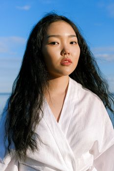 在明亮的蓝天下，一位优雅的亚洲女子正在户外摆姿势