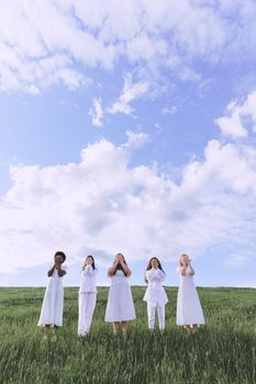 在蓝天下的田野里，身着白色连衣裙的女性们一起摆姿势