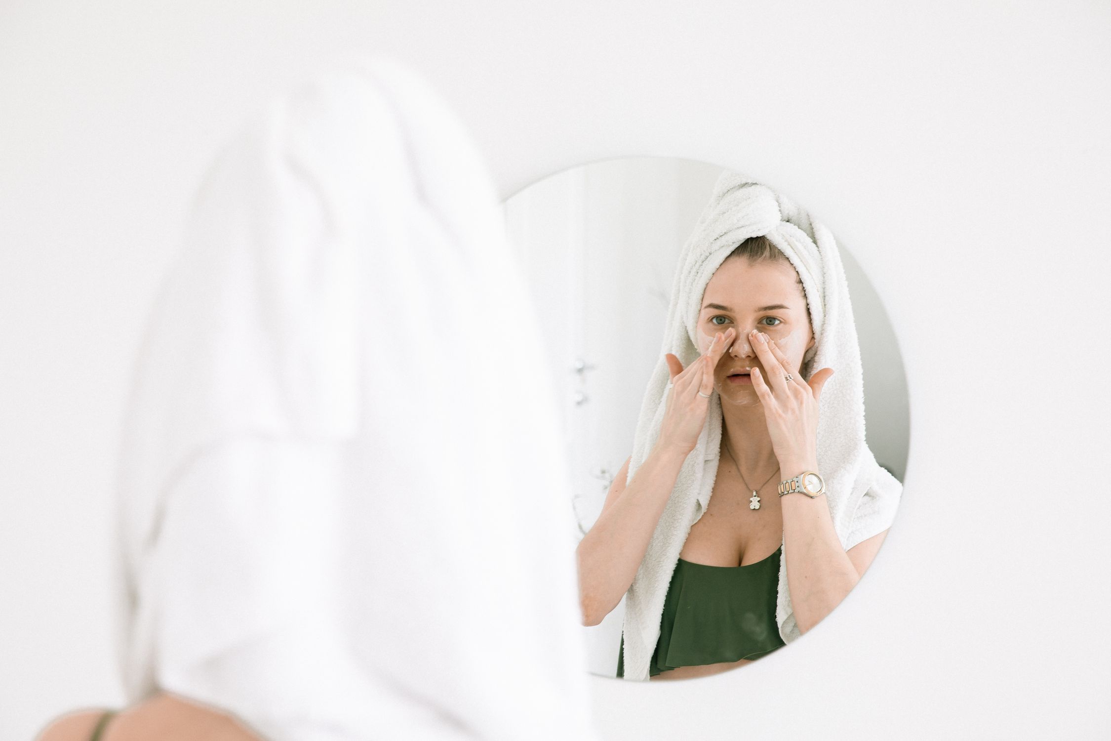 Woman in a towel performing her skincare routine in front of a bathroom mirror while traveling