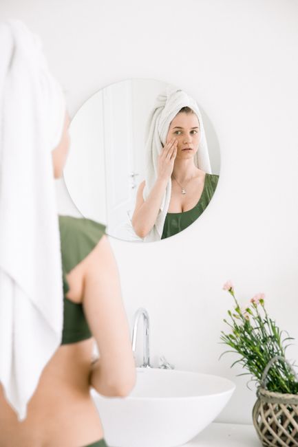 A woman with a towel headwrap applies skincare in a stylish bathroom.