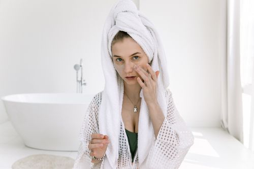 Free Woman in a bathrobe applying skincare cream in a bright spa-like setting. Stock Photo