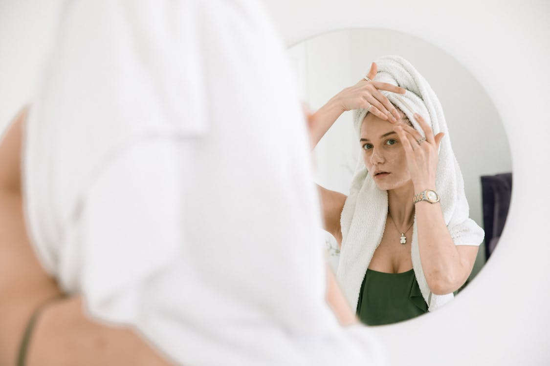 Woman Standing In front Of A Mirror Applying Cream On Her Face