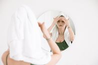女人头上戴着毛巾，对着镜子进行护肤程序