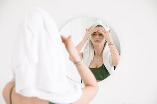女人头上戴着毛巾，对着镜子进行护肤程序