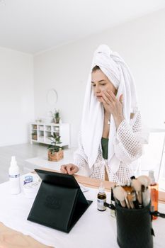 Woman in bathrobe applying skincare in a modern bathroom setting with beauty products.