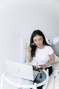 A woman applies makeup while participating in a video call, showcasing a modern beauty routine.