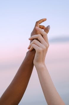 Two diverse hands holding together, symbolizing unity and friendship at sunset.