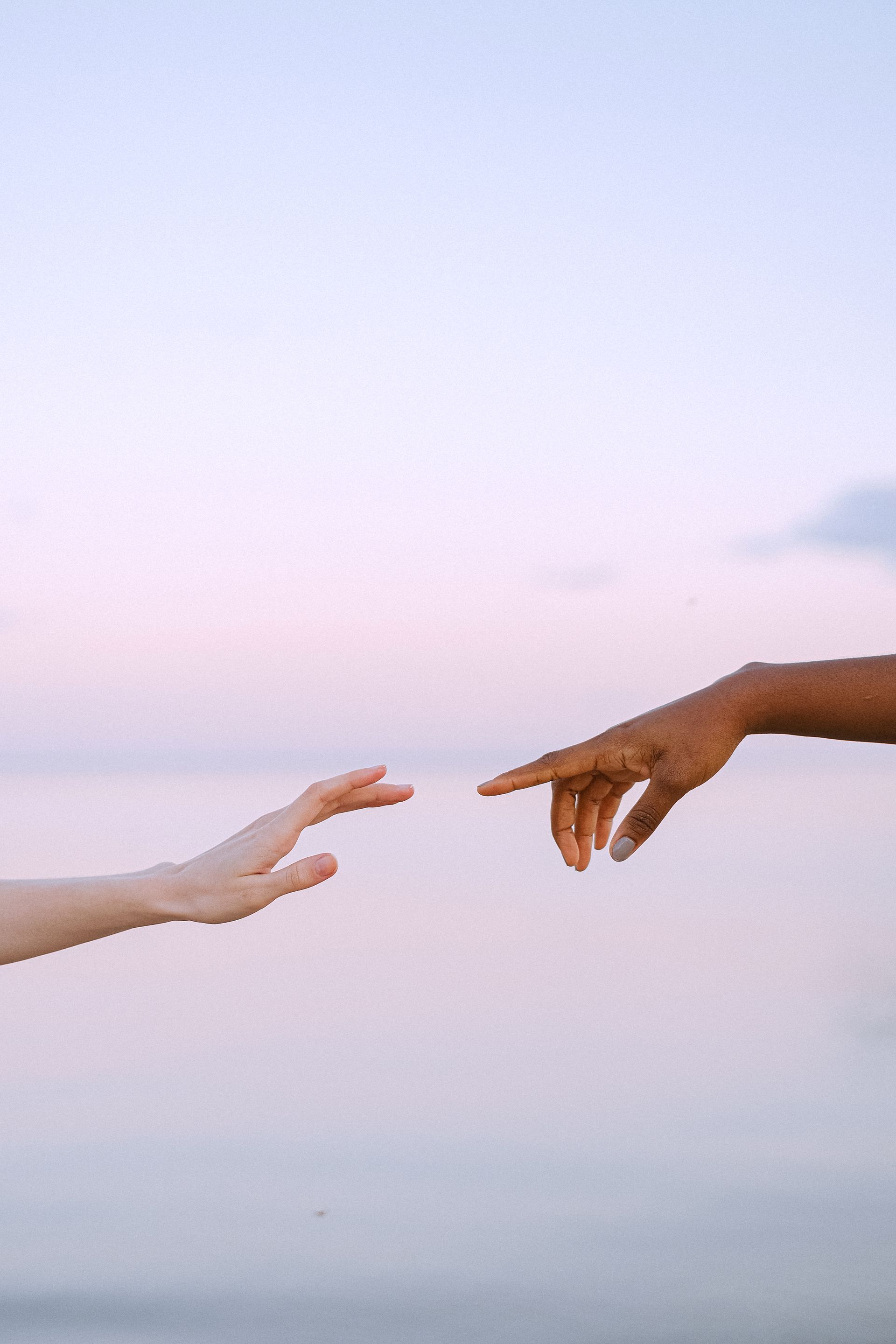 Two hands reaching toward one another beneath a pale evening sky