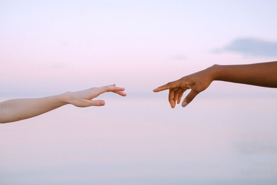 Two hands reaching toward each other against a pale sky — photo by Anna Shvets on Pexels