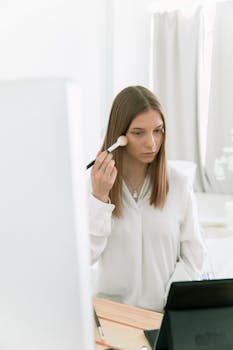 Young woman applying makeup using a brush, focusing on self-care and beauty routine.