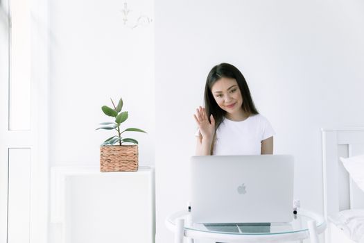 在一间明亮、极简风格的空间里，一名年轻女子正远程工作，她对着笔记本电脑屏幕挥手致意
