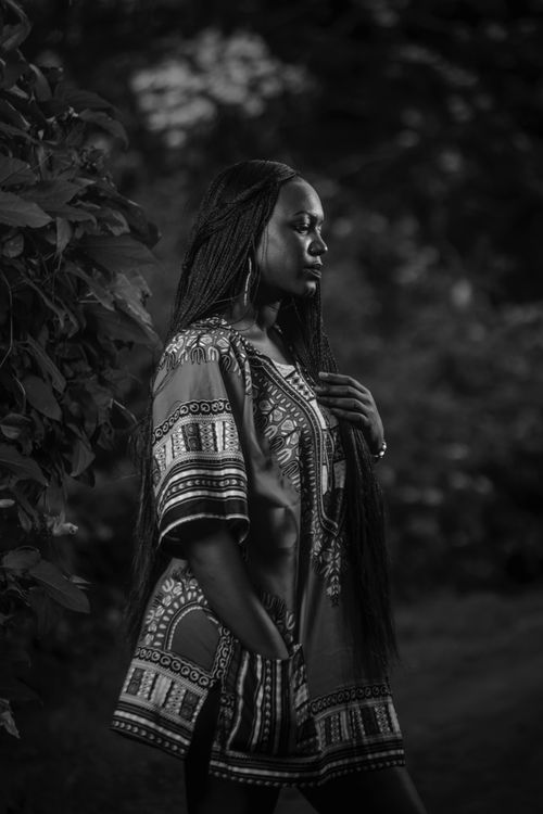 Free Black and white side view of young serious African female with long pigtails in traditional dress standing near plants Stock Photo