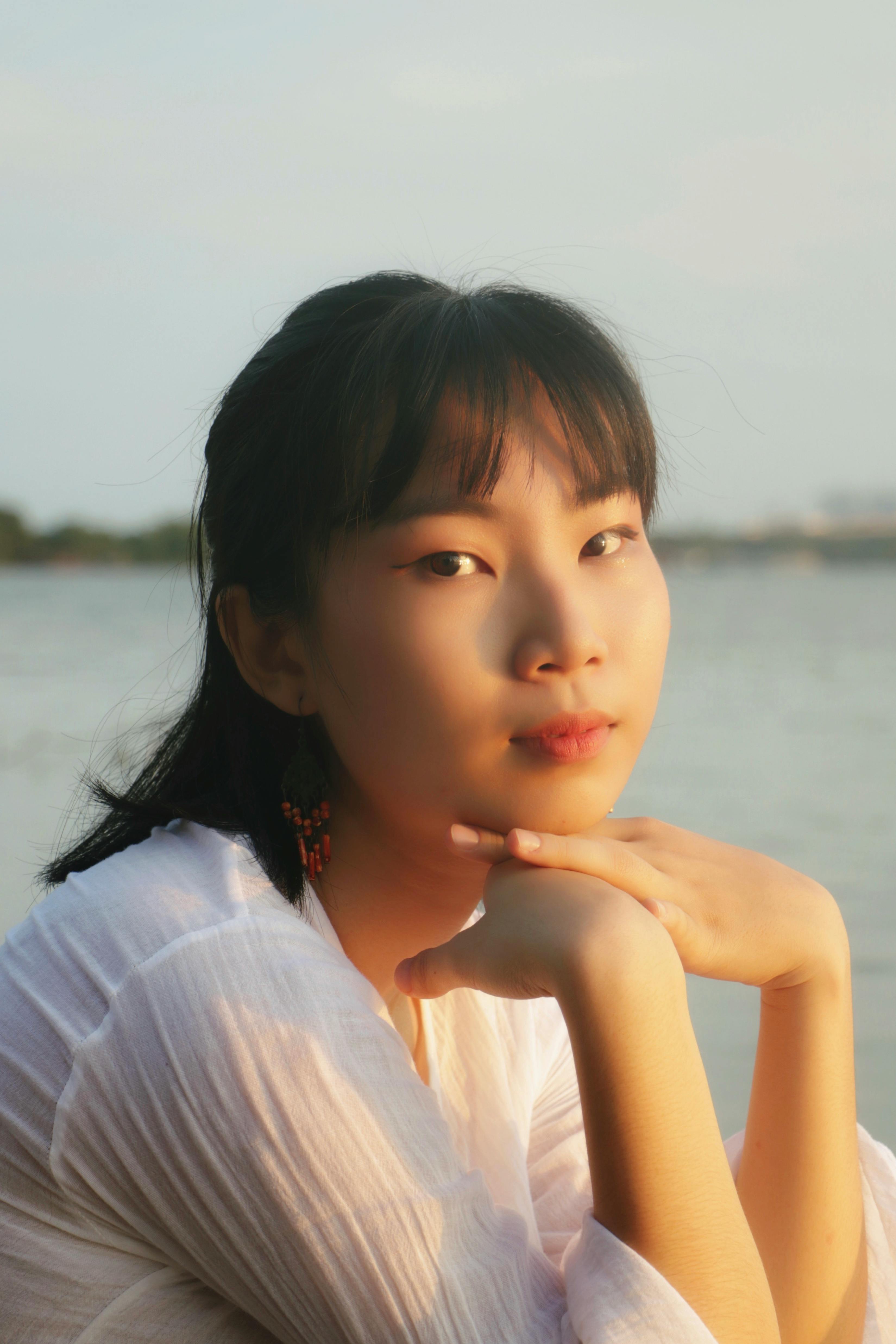 A serene portrait of a young woman posing outdoors by the water during daylight.