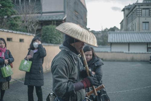 Free An Asian man plays a bamboo flute on a quaint street, captivating onlookers. Stock Photo