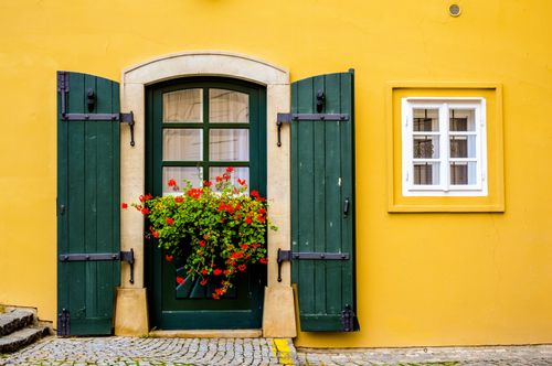 Free Vibrant yellow wall with a classic green wooden door and red flowers, embodying European charm. Stock Photo