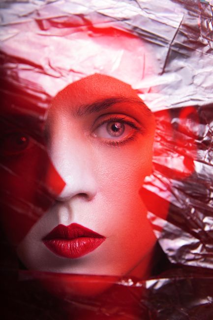 Close-up portrait of a woman with striking red lips framed by shiny foil, creating an artistic and vibrant effect.