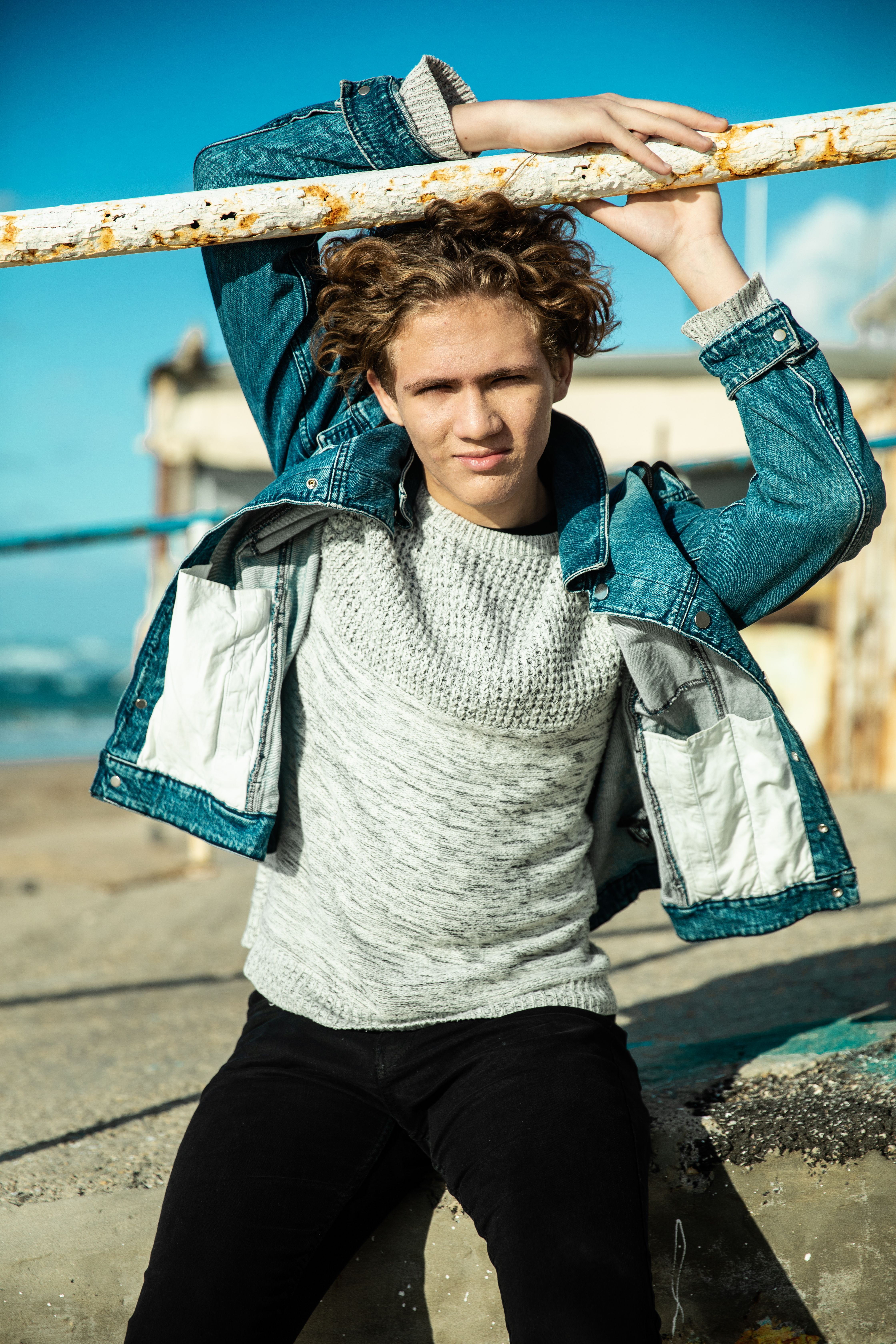 Casual portrait of a young man sitting outdoors in denim jacket.