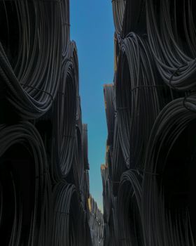 Vertical shot of piled steel bars in warehouse against a clear blue sky.
