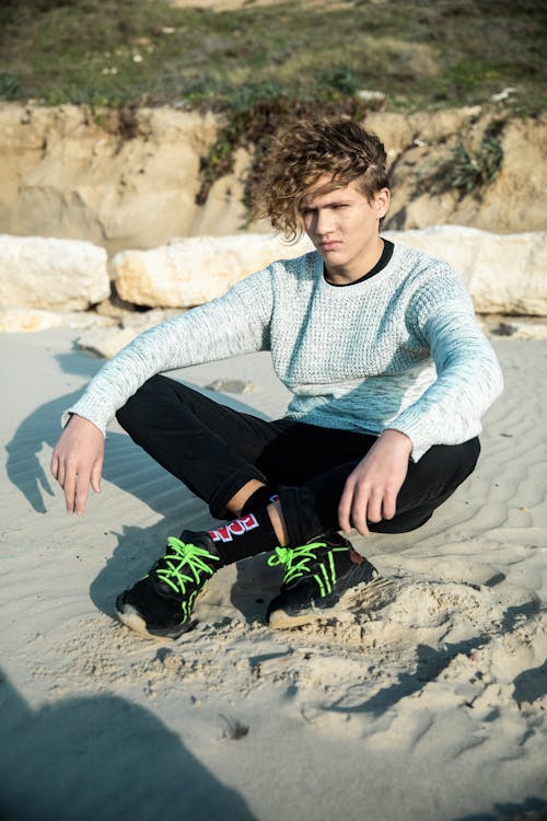 Man in Gray Sweater and Black Pants Sitting on a Sand