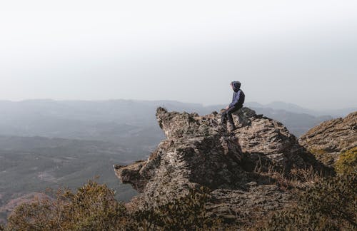 Man in Blue Jacket Sitting on a Rock Formation