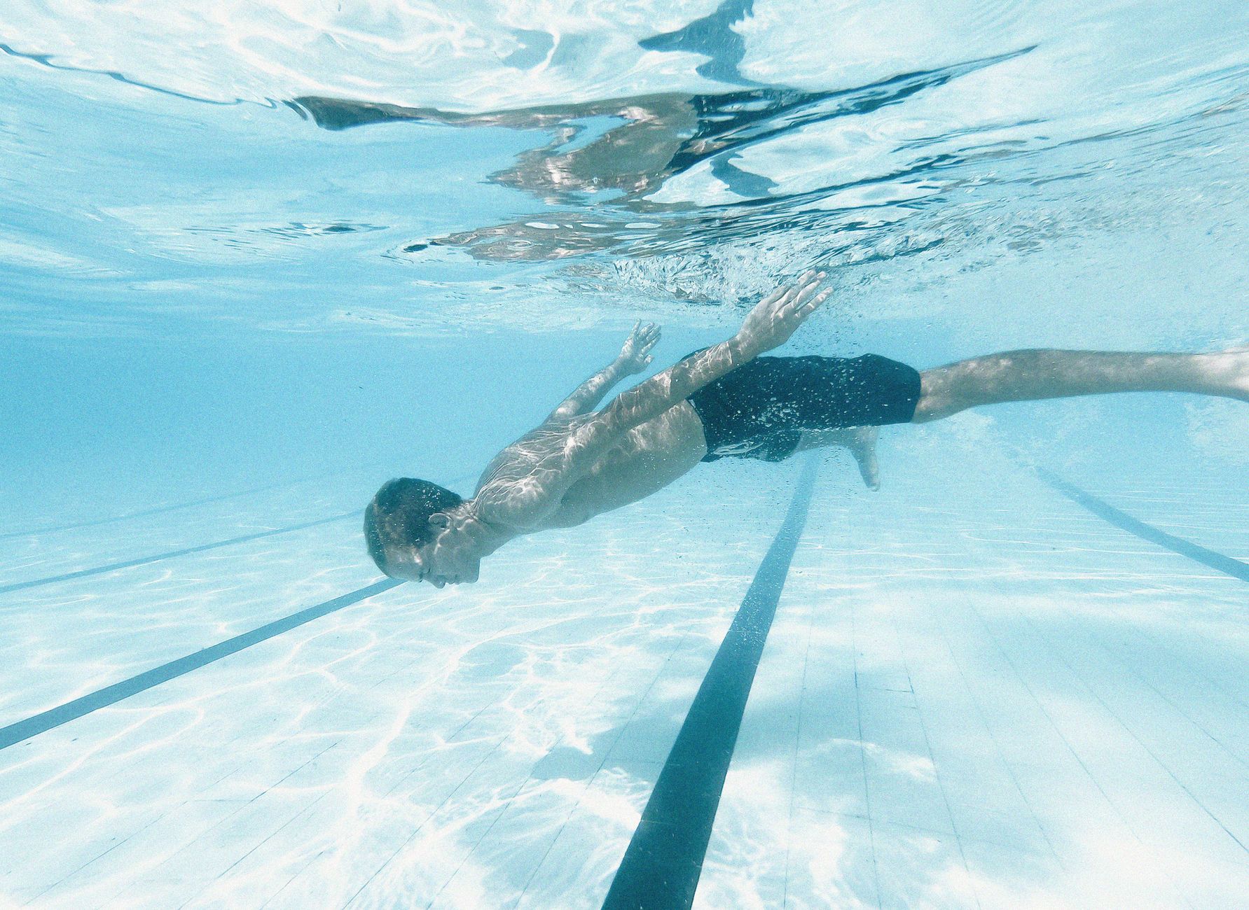 A man swimming underwater in a clear swimming pool, showcasing diving action.