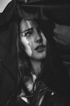 Artistic black and white close-up portrait of a woman with expressive gaze and shadows.
