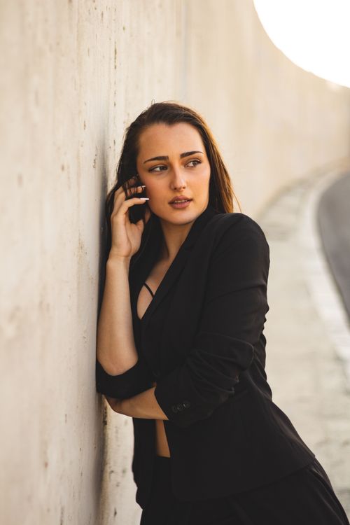 Free Elegant woman in black suit posing against a concrete wall outdoors, exuding confidence and style. Stock Photo