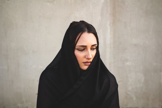 A serene portrait of a woman wrapped in a black scarf, set against a muted background.
