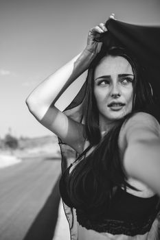 Striking black and white portrait of a woman in lingerie posing outdoors in natural light.