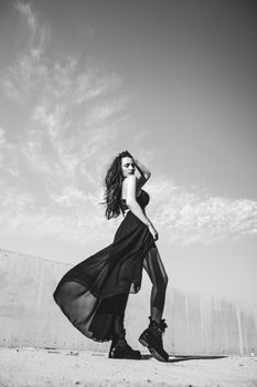 Black and white photo of a fashionable woman posing in a flowing dress outdoors.