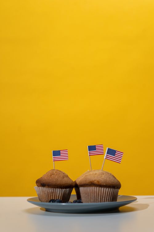 Free Two muffins decorated with American flags on a plate against a yellow backdrop, perfect for patriotic celebrations. Stock Photo