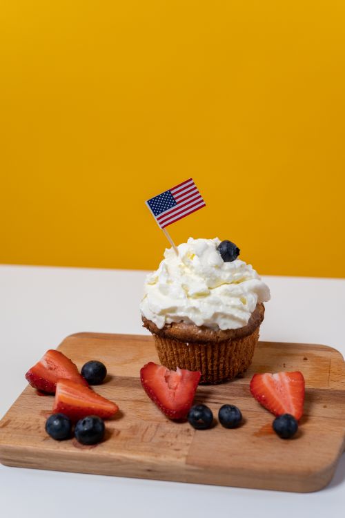 Free Festive cupcake topped with whipped cream, blueberries, and a U.S. flag, on a wooden board. Stock Photo