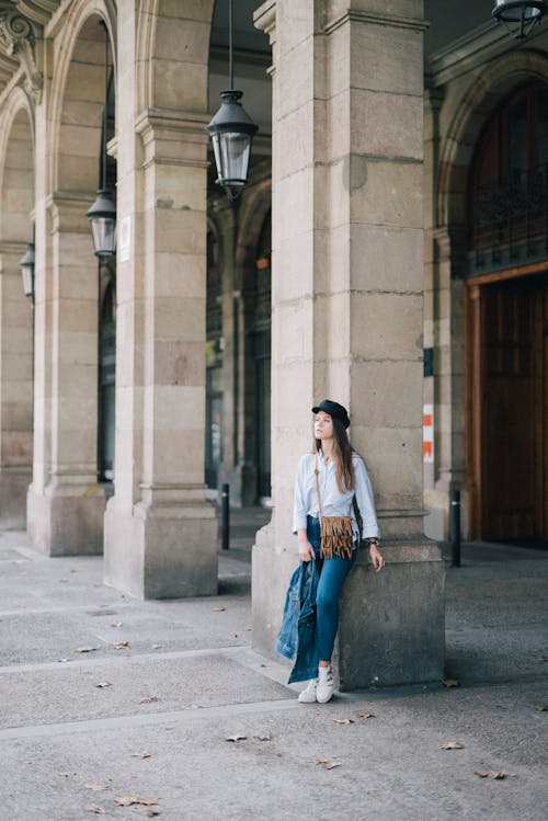 Mujer En Camisa De Manga Larga Blanca Y Marrón Y Pantalones Vaqueros Azules De Pie Sobre Hormigón Gris