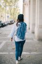 一名身穿牛仔夹克、头戴贝雷帽的女子，正走在城市的人行道上，留下一个背影