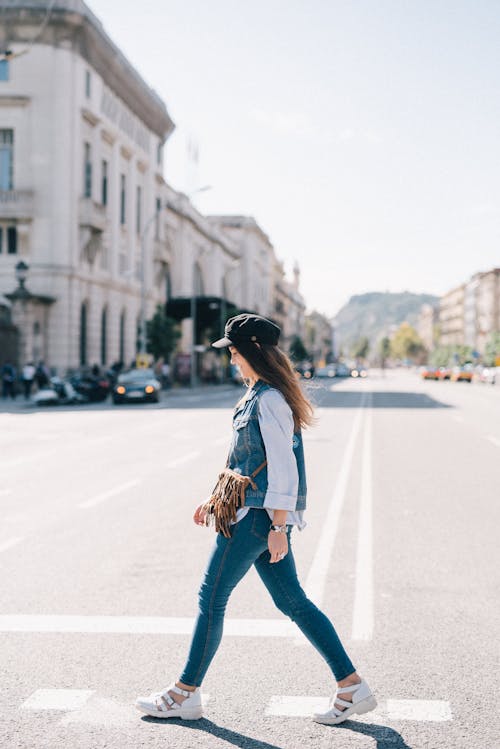 白衬衫和蓝色牛仔牛仔裤，戴着黑帽子站在路上的女人