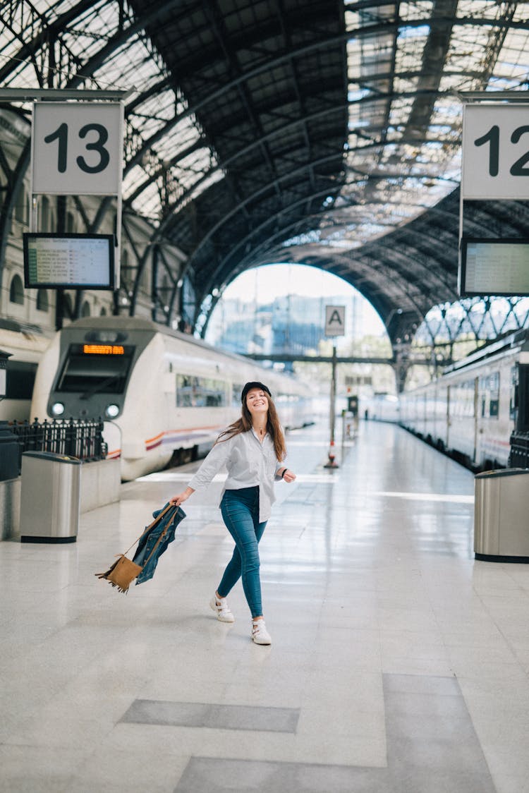 Woman In White Long Sleeve Shirt And Blue Denim Jeans Standing On The Platform Of A Train Station