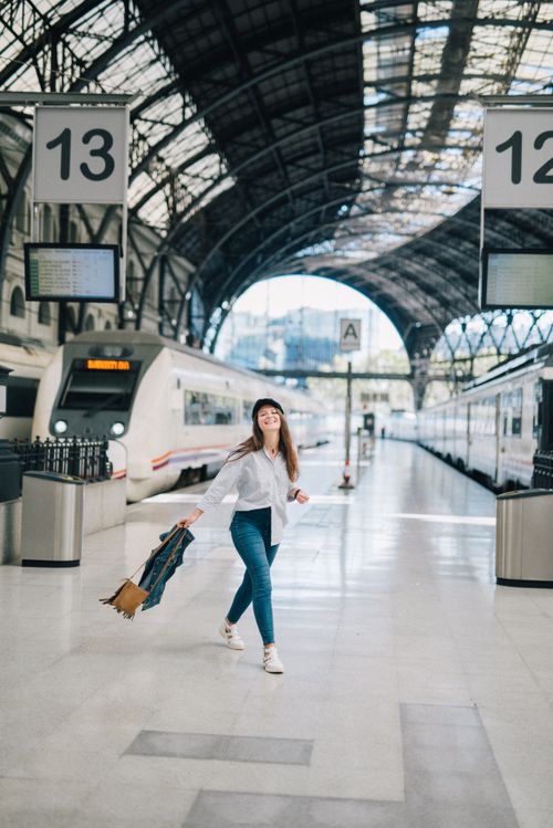 Free Smiling woman walks with luggage in a modern train station, showcasing travel and mobility. Stock Photo