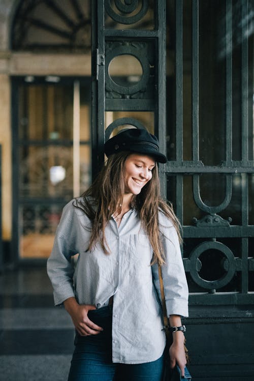 Free Woman in White Long Sleeve Shirt and Black Hat Standing Near Black Metal Gate Stock Photo
