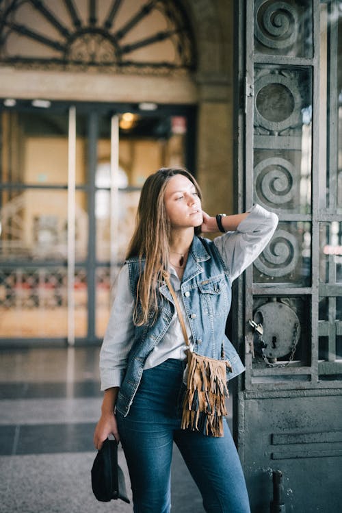 Woman in Blue Denim Button Up Jacket Standing Near An iron Gate