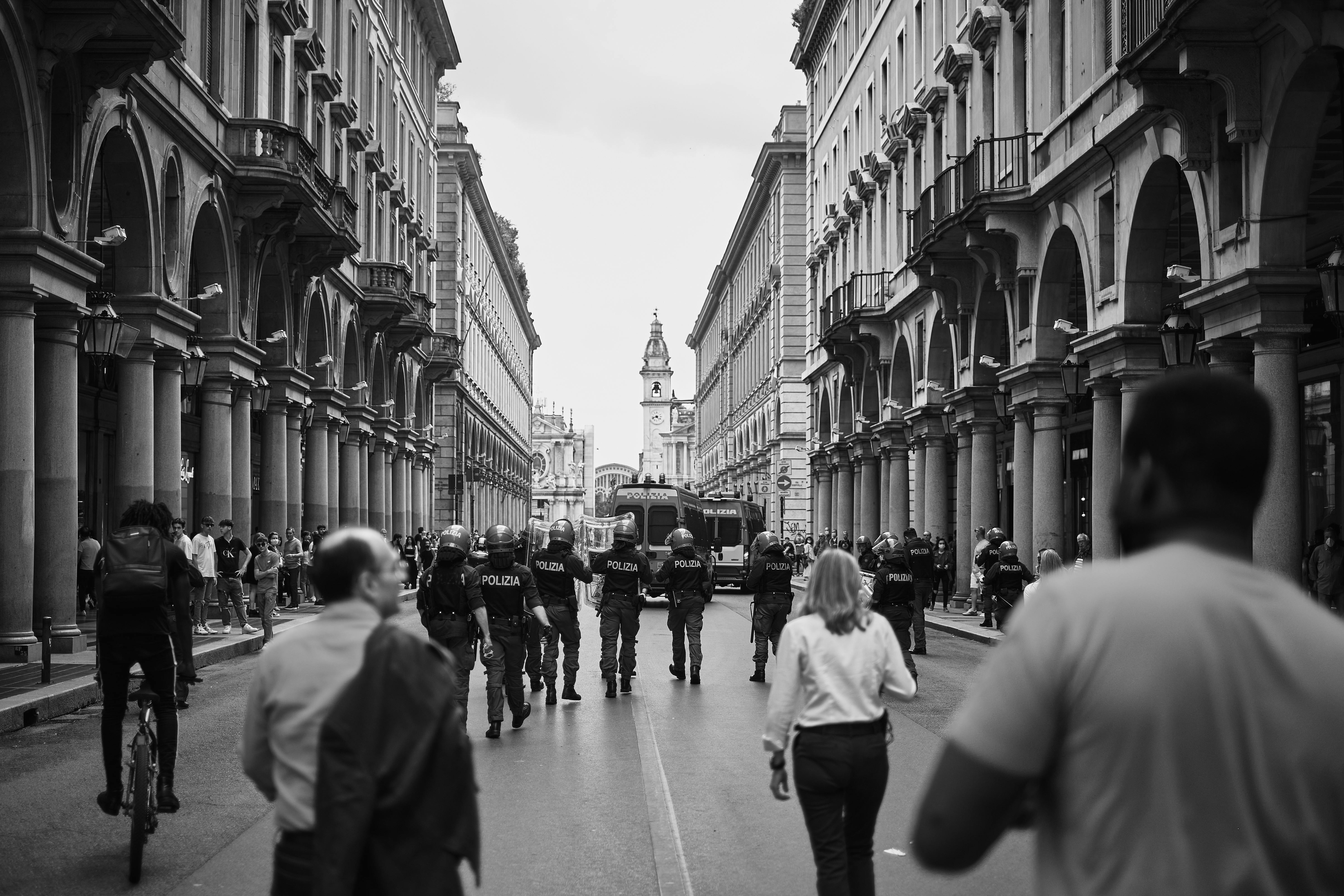 A dynamic street protest in Torino, Italy, captured in monochrome highlighting police presence and urban architecture.