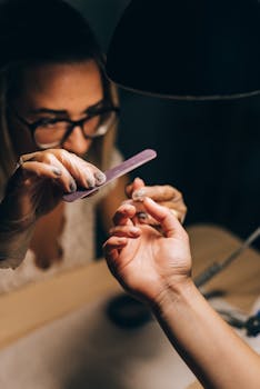A detailed view of a manicurist filing a woman's nails under soft lighting.