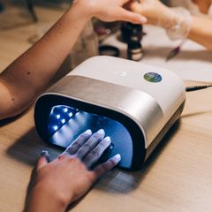 Hand curing gel nails inside a white and silver nail lamp with a lit timer on its top